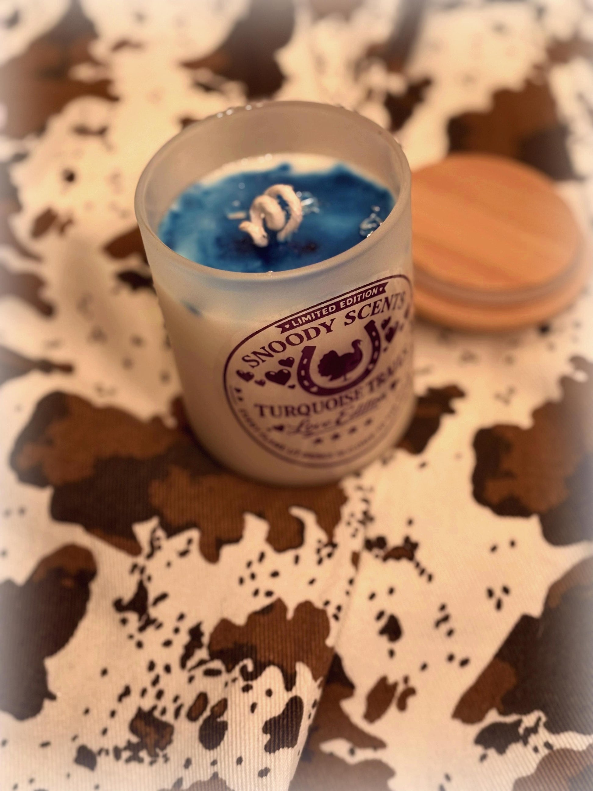 Open candle jar showing blue wax with a foil-wrapped jewelry surprise inside, wood lid resting alongside