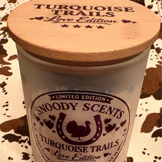 Close-up of the Snoody Scents Turquoise Trails Love Edition candle label and wood lid on cowhide print fabric