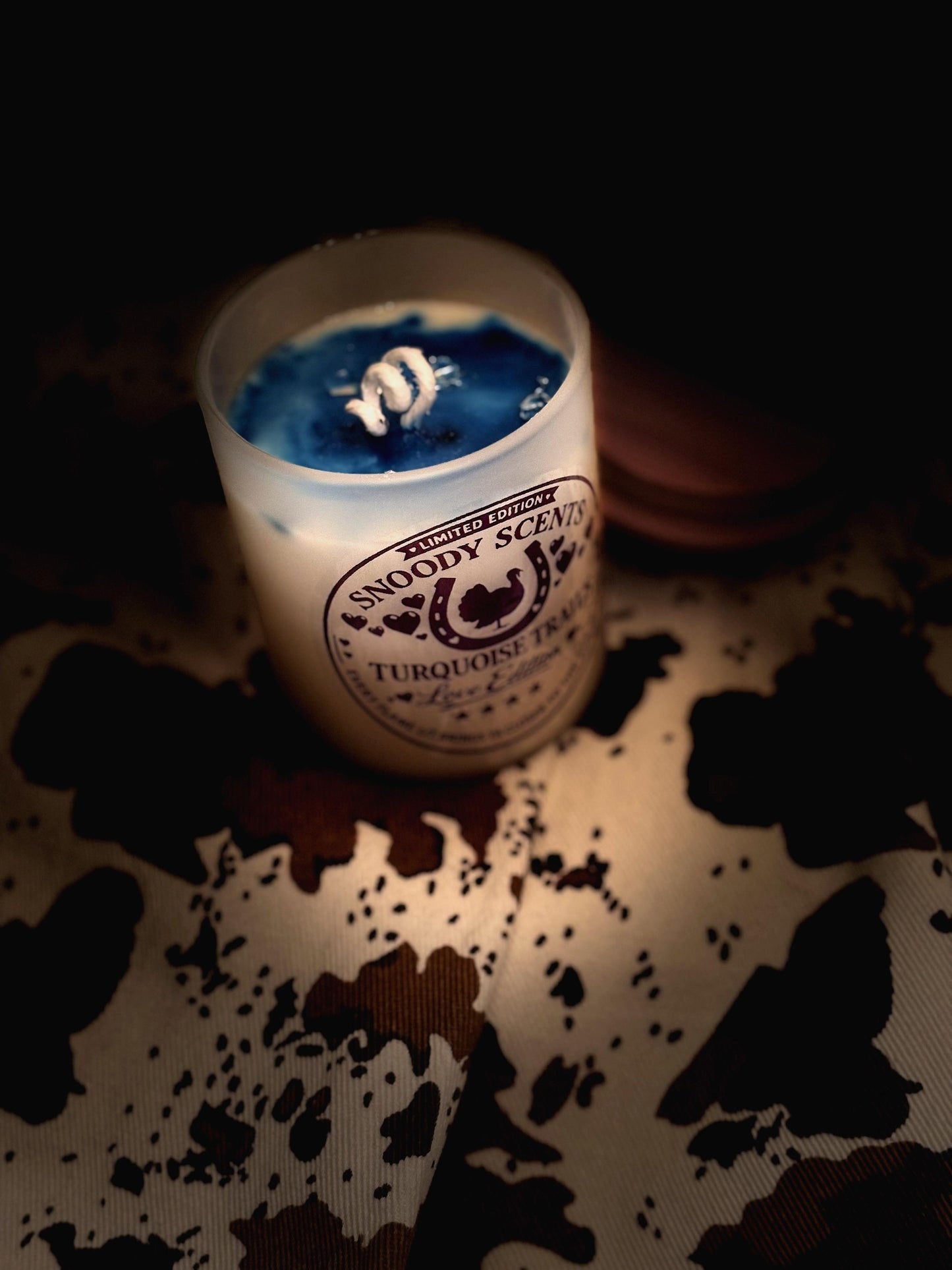 Turquoise Trails candle with blue wax and hidden jewelry packet lit dramatically on cowhide print fabric